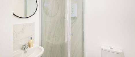 Een badkamer met een douchecabine van glas, een witte wastafel met een marmeren achterwand, en een toilet.