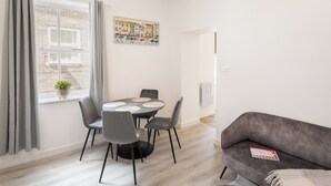 Una sala de estar moderna con un sofá gris, una mesa de comedor con cuatro sillas, una planta en maceta y un cuadro en la pared.