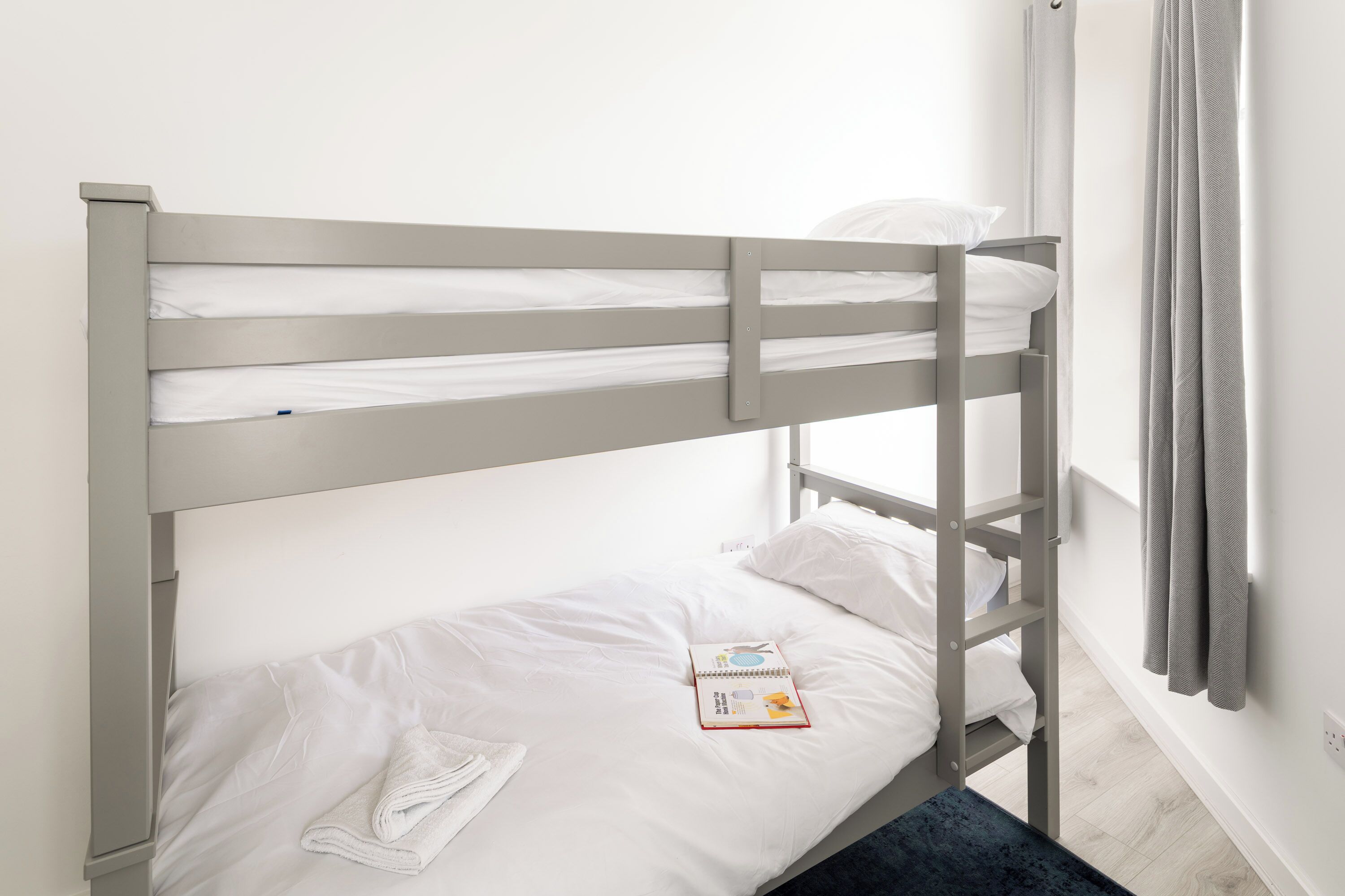 Uma cama de beliche com roupa de cama branca e um livro na cama inferior.