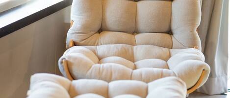 A tufted armchair with wooden legs in a room with a large window and curtains.