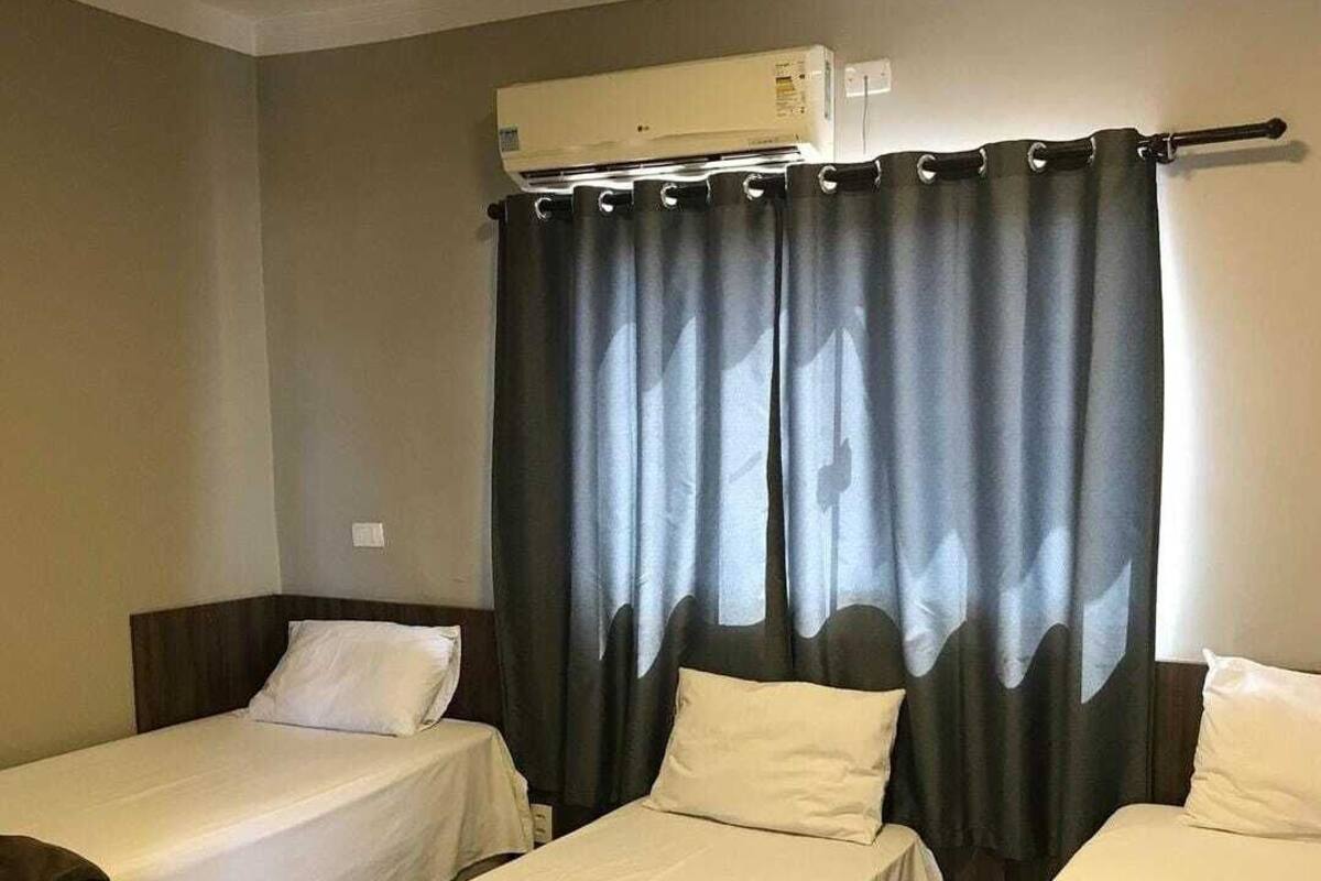 A hotel room with two single beds, a table with a towel, and a window with curtains.
