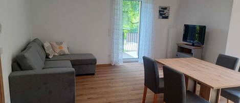 Una sala de estar moderna con un sofá seccional gris, una mesa de comedor de madera con cuatro sillas y un televisor sobre un mueble.