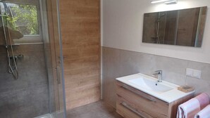 Un baño moderno con cabina de ducha de vidrio, un tocador de madera con lavabo blanco y un espejo grande encima.