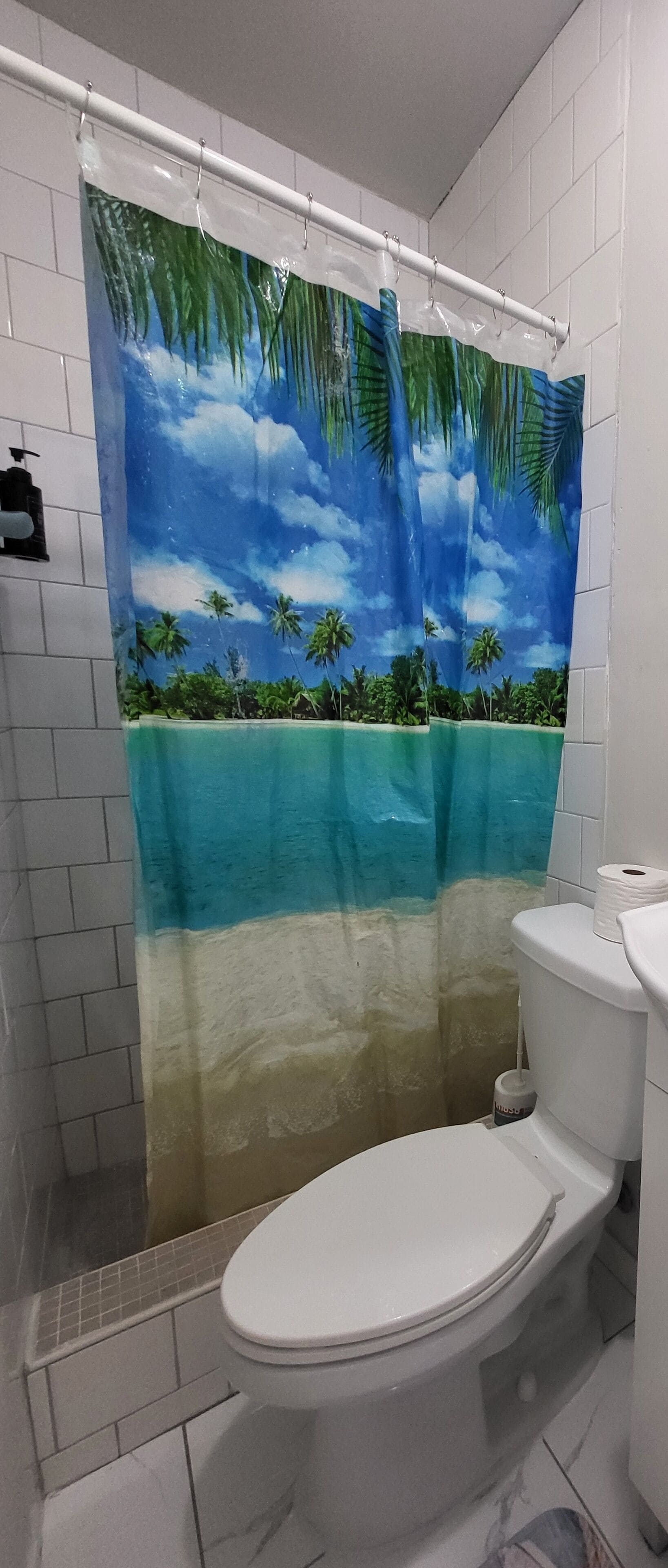 Ein Badezimmer mit Toilette, einer Duschkabine mit tropischem Strandmotiv und einer Toilettenbürste.