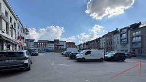 Un parking avec des véhicules, des bâtiments et un ciel dégagé.