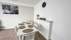 A dining area with a white table and chairs, a clock on the wall, and a shelf with decorative items. - Tirou 3 station and airport center (Charleroi)