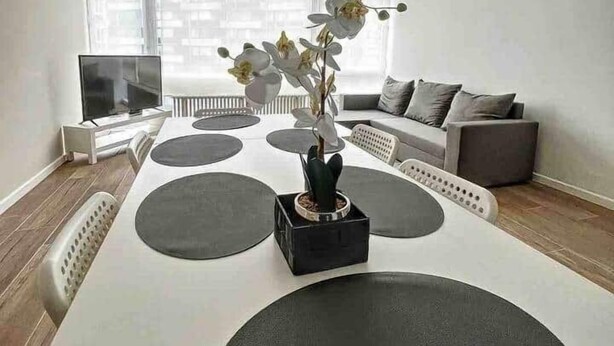 Ein modernes Wohnzimmer mit einem weißen Sofa, einem schwarzen Couchtisch mit Orchidee im Topf und einem großen Fenster.
