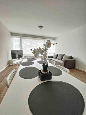 A modern living room with a white sofa, a black coffee table with a potted orchid, and a large window. - Tirou 5 center - train station - airport (Charleroi)