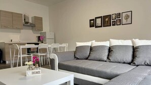 Ein modernes Wohnzimmer mit grauem Sofa, weißem Couchtisch und einer Küchenzeile im Hintergrund.
