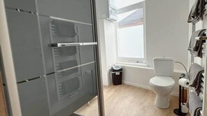 Ein modernes Badezimmer mit Duschkabine aus Glas, Toilette, Mülleimer und einem Fenster für natürliches Licht.