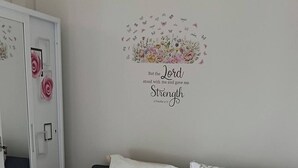 Un dormitorio con cama, sofá con cojines florales, pared con diseño floral y una cita, y puerta con espejo.
