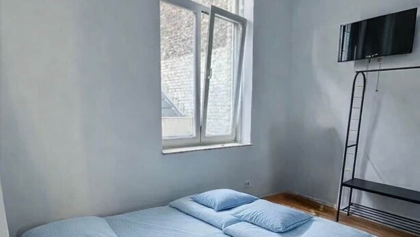 Un dormitorio con cama, almohadas, ventana, televisión y radiador.