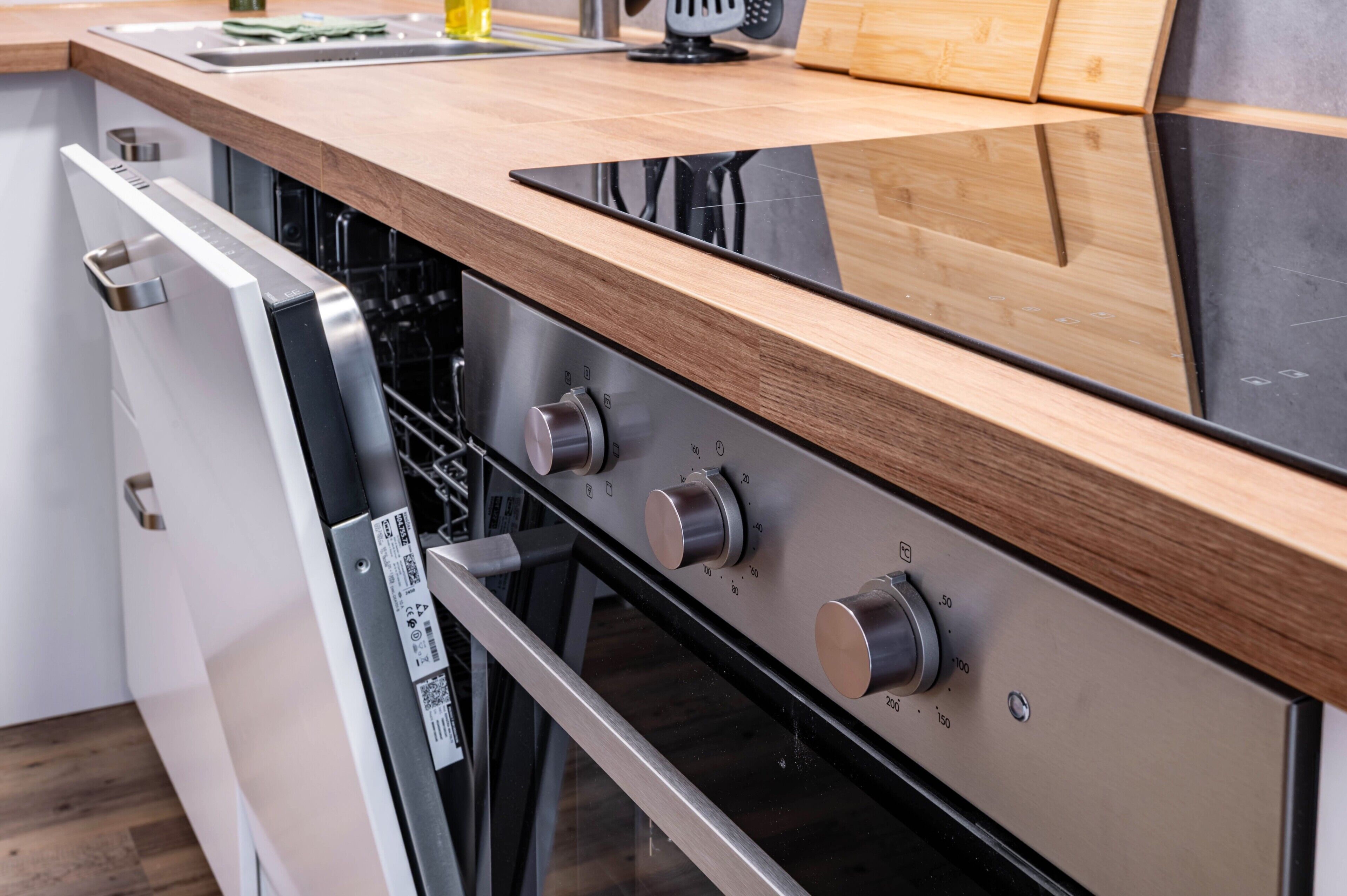 Une cuisine équipée d’un lave-vaisselle, d’un four et d’un plan de travail en bois.