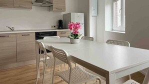 A modern kitchen with wooden cabinets, a white countertop, a dining table with four chairs, and a window with blinds.