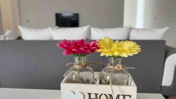 Ein weißer Tisch mit einer Holzkiste, auf der 'HOME' steht, und zwei Glasflaschen mit Blumen.