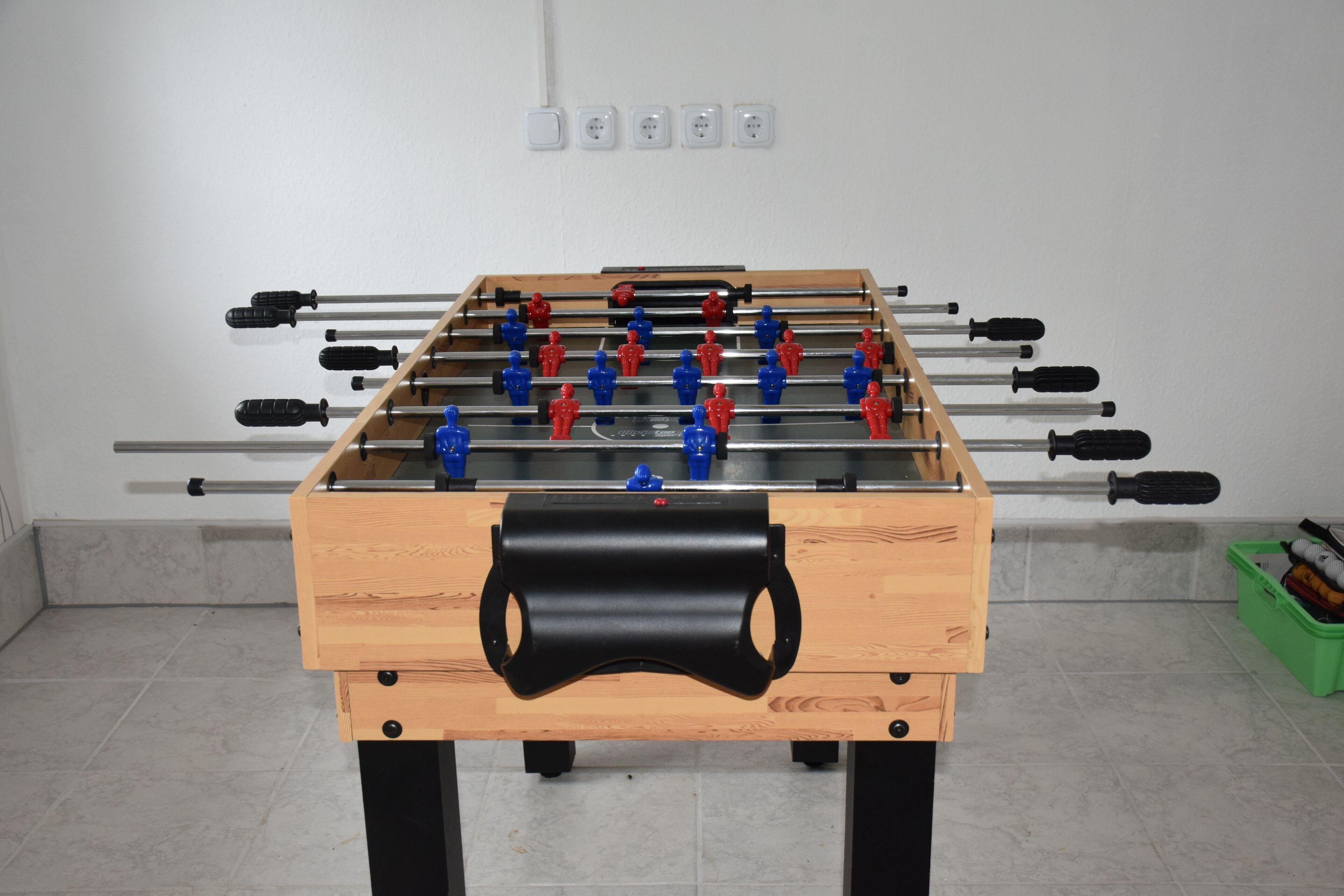 Un tavolo da calcio in una stanza con pavimento piastrellato e un tavolo di legno.