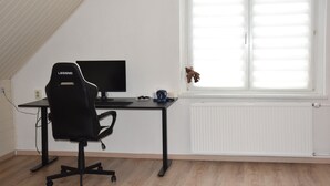 Une pièce avec un fauteuil de jeu noir, un bureau avec un ordinateur et une fenêtre avec des stores.
