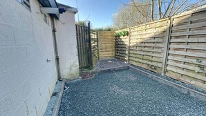 Un espace extérieur clos, avec un sol en gravier, des murs en bois et un portail en métal.