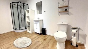 Une salle de bain avec une douche à parois de verre, un lavabo blanc, des toilettes et une étagère contenant des articles de toilette.