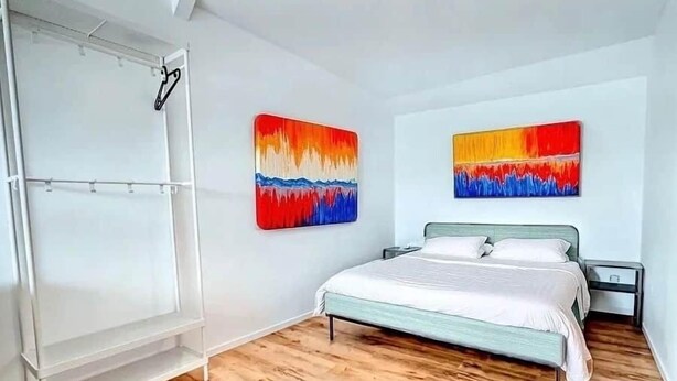 Une chambre à coucher comprenant un lit, une armoire et deux tableaux abstraits accrochés au mur.