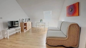 Un salon moderne avec un téléviseur à écran plat, un meuble en bois, une table à manger blanche et un canapé en osier.