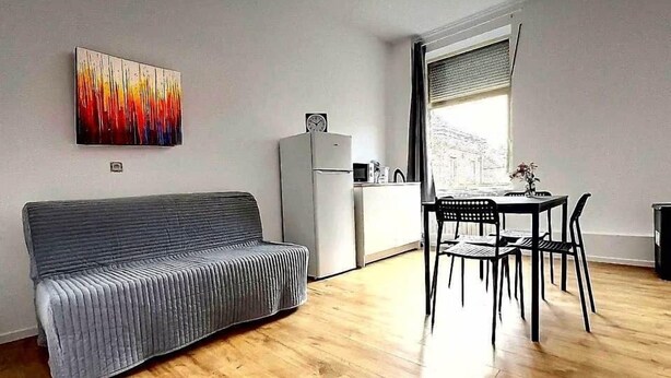 A compact living space with a sofa, a dining table with chairs, a kitchenette, and a window with blinds.