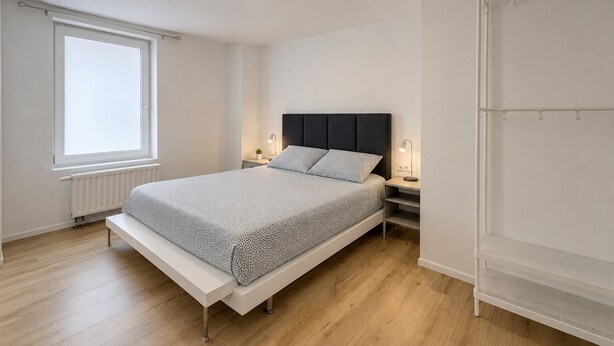 A bedroom with a bed, bedside tables, a window, and a radiator.