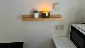Et køkken med en træhylde, hvor der står en potteplante og et lys, samt en mikrobølgeovn og en stikkontakt.
