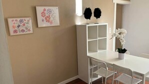 Et lille spiseområde med et hvidt bord og stole, et hvidt skab samt to billeder af blomster på væggen.