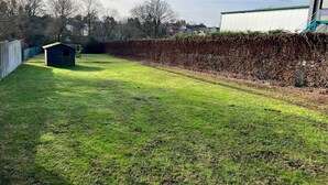 Un espace extérieur verdoyant, avec un petit abri de jardin, un mur en pierre et un bâtiment doté d’un toit végétalisé.