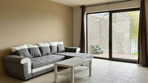 A modern living room with a grey sectional sofa, a white coffee table, and a large sliding glass door leading to a brick patio.