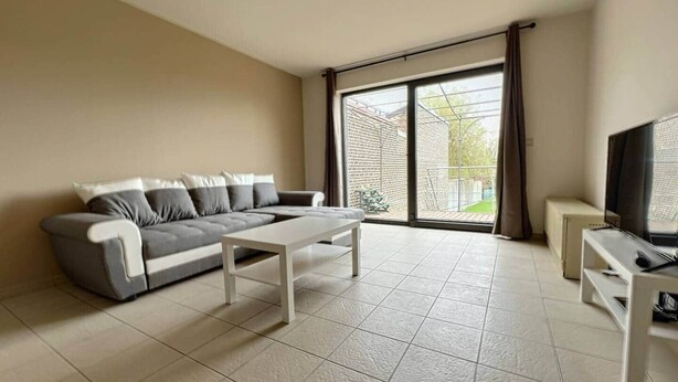 A living room with a sofa, a coffee table, a TV, and a sliding glass door leading to a patio.