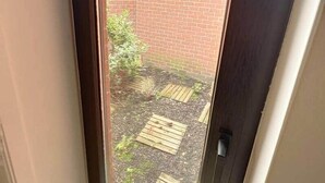 A view through a door into a brick courtyard with a wooden deck and a small plant.