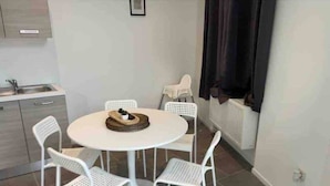 A dining area with a round table and four white chairs, a small kitchen area with a sink and cabinets, and a radiator on the wall.