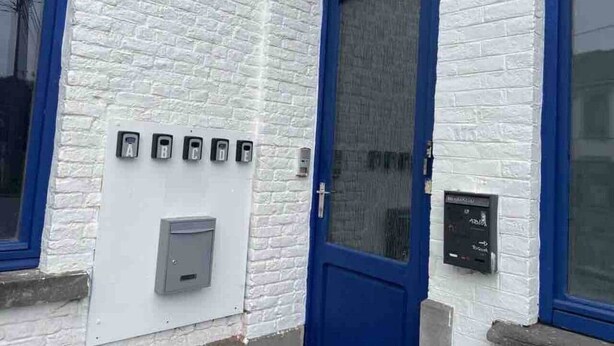 A building with a white brick exterior, a blue door, and a mail slot.