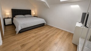 A bedroom with a bed, nightstands, a TV, and a skylight.