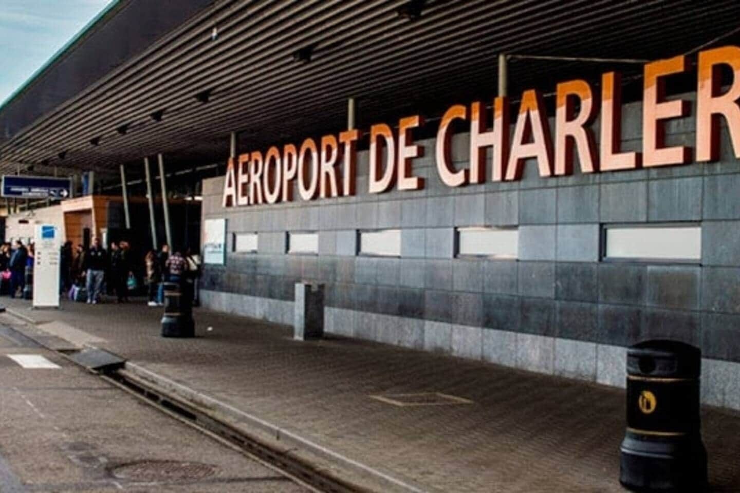 The exterior of the Airport de Charler, featuring a prominent sign, a covered waiting area, and a paved walkway.