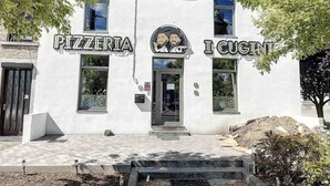 Un edificio con letreros que dicen 'PIZZERIA' y 'I CUGNIT', una puerta y un escalón pequeño que lleva a la entrada.