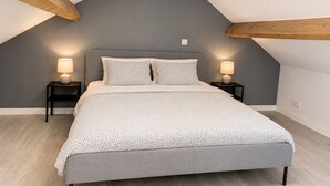 Un dormitorio con techo inclinado, una cama con colcha estampada, dos lámparas de noche y vigas de madera.