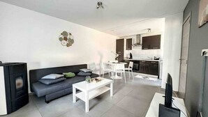 Una sala de estar moderna con sofá, mesa de centro y chimenea. Se observa un comedor con sillas y una cocina al fondo.