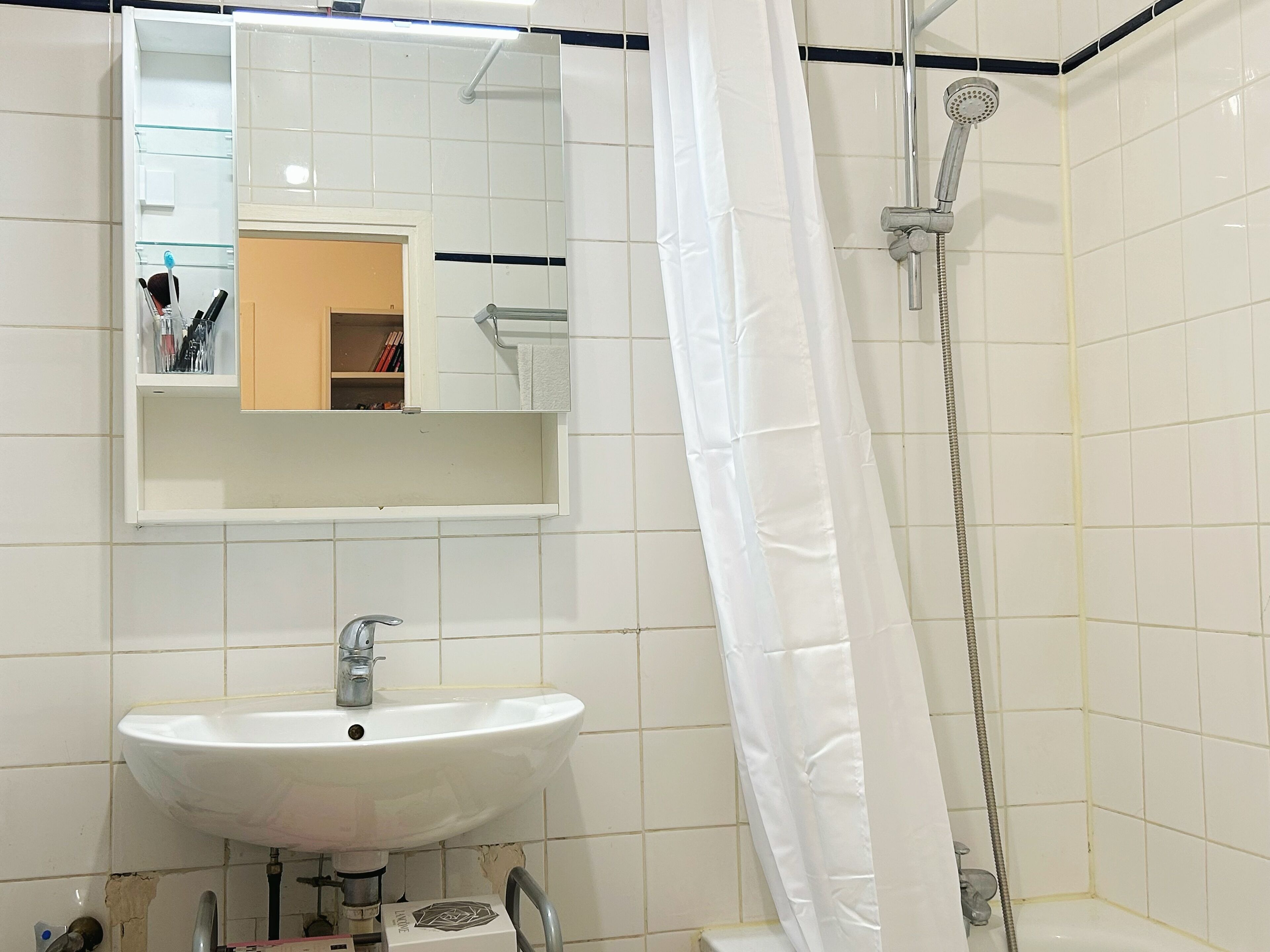 Une salle de bain avec un lavabo blanc, un miroir et une douche.