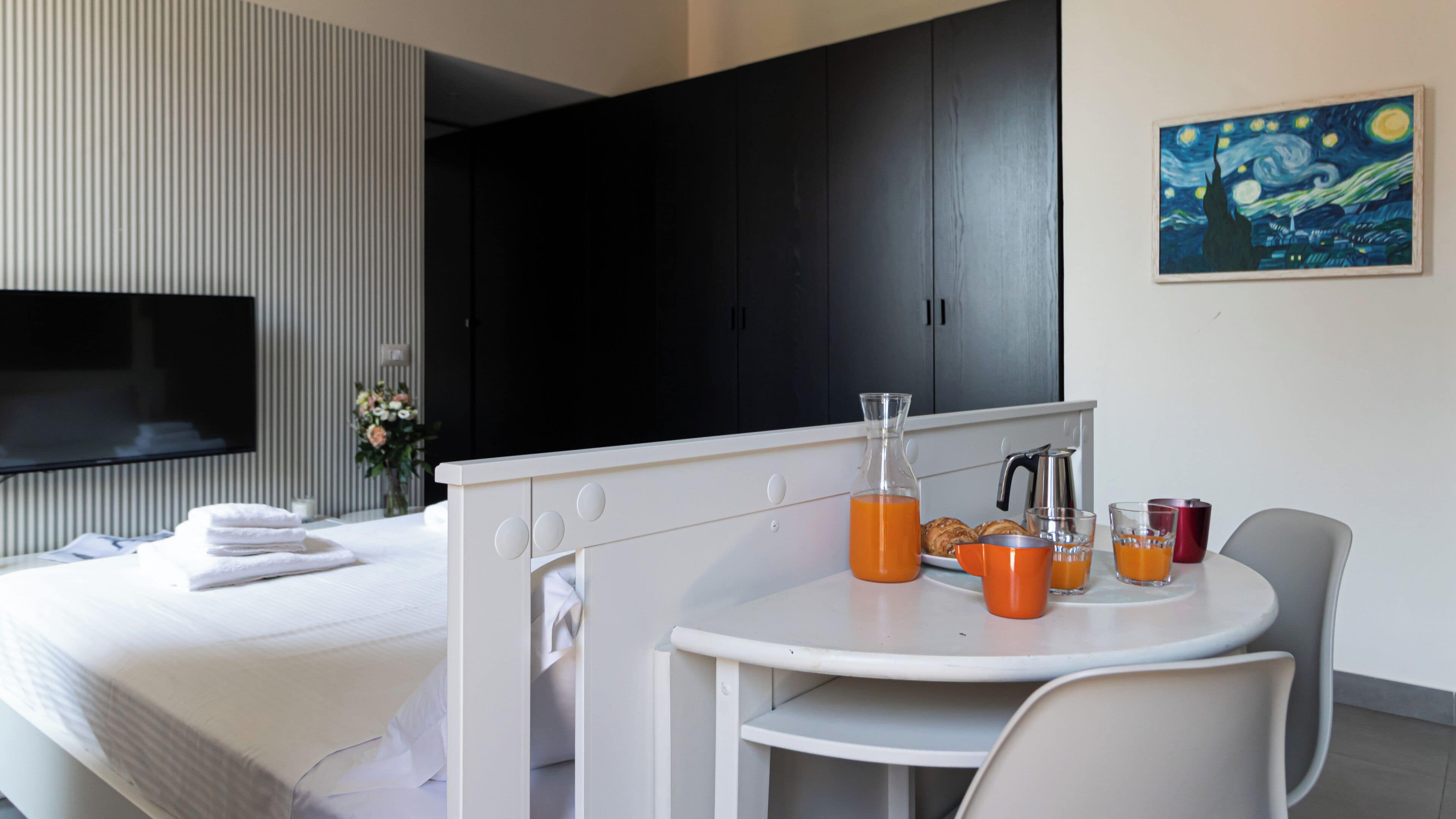 Une chambre d’hôtel moderne comprenant un lit, une petite kitchenette, un coin repas avec une table et des chaises, et un tableau accroché au mur.