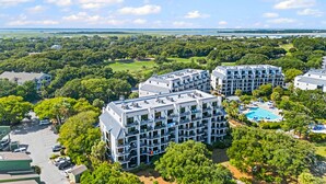 A multi-story hotel with balconies, a swimming pool, and a golf course in the background.
