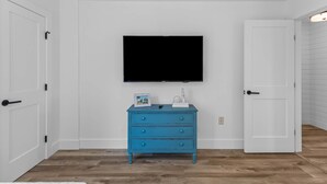 A room with white walls, a blue dresser, a flat-screen TV, and a white door.