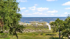 A coastal landscape with a clear view of the sea, a grassy path, and trees.