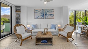 A modern living room with a white sofa, two wicker chairs, a coffee table, and a ceiling fan.