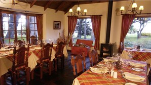 A dining area with tables set for a meal, wooden chairs, and a fireplace. - Hosteria Helsingfors (Estancia Helsingfors)