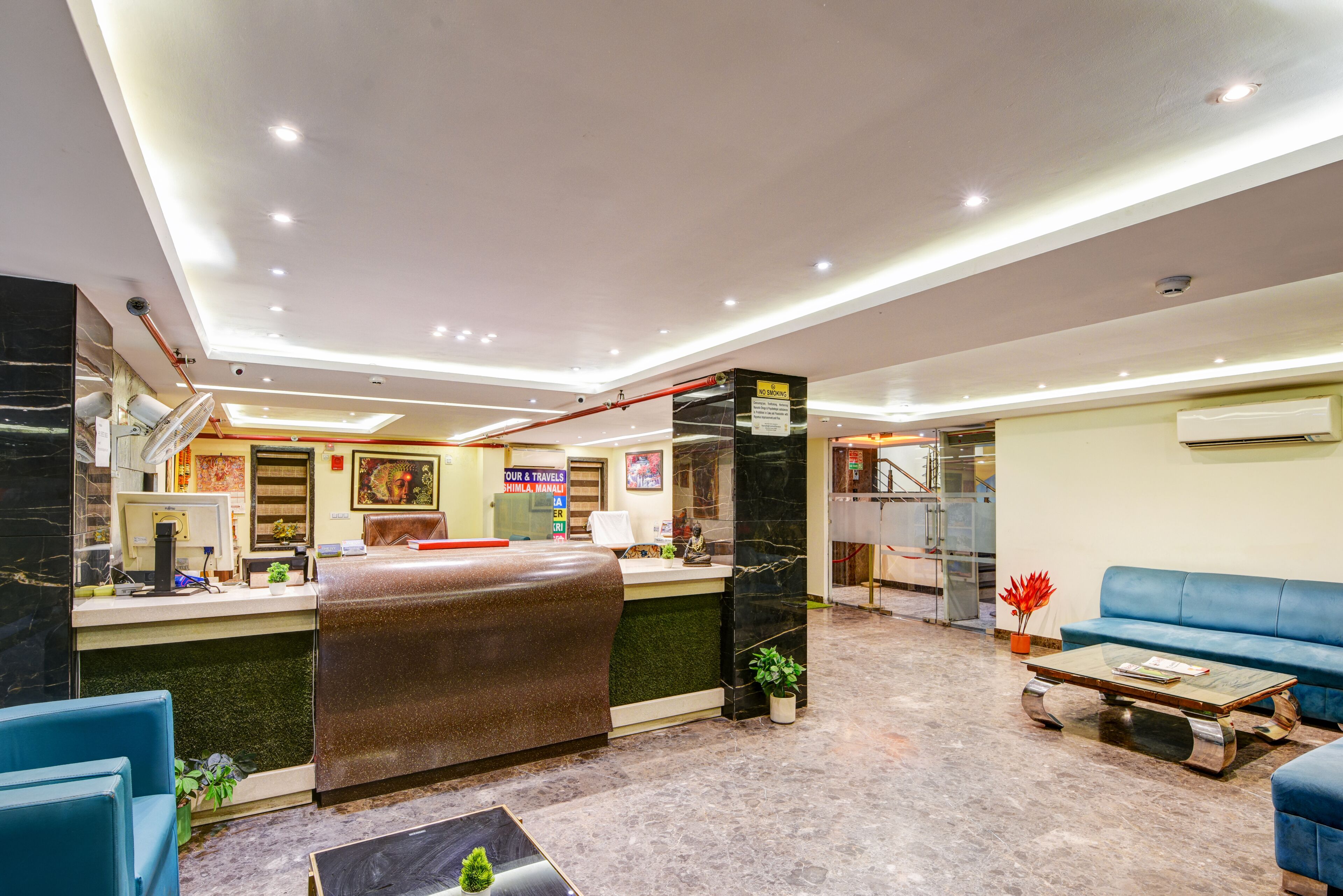Een hotel lobby met een receptiebalie, een zithoek en een trap naar een verdieping erboven.