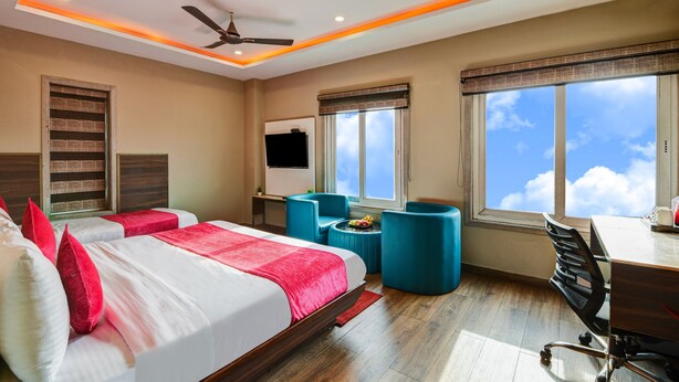 Ein Hotelzimmer mit zwei Betten, einem Schreibtisch, einem Sessel, einem Fernseher und großen Fenstern mit Blick zum Himmel.