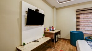 Ein modernes Zimmer mit einem an einer weißen Wand montierten Flachbildfernseher, einem Holztisch mit einem kleinen Topfpflanzen und einem blauen Hocker.